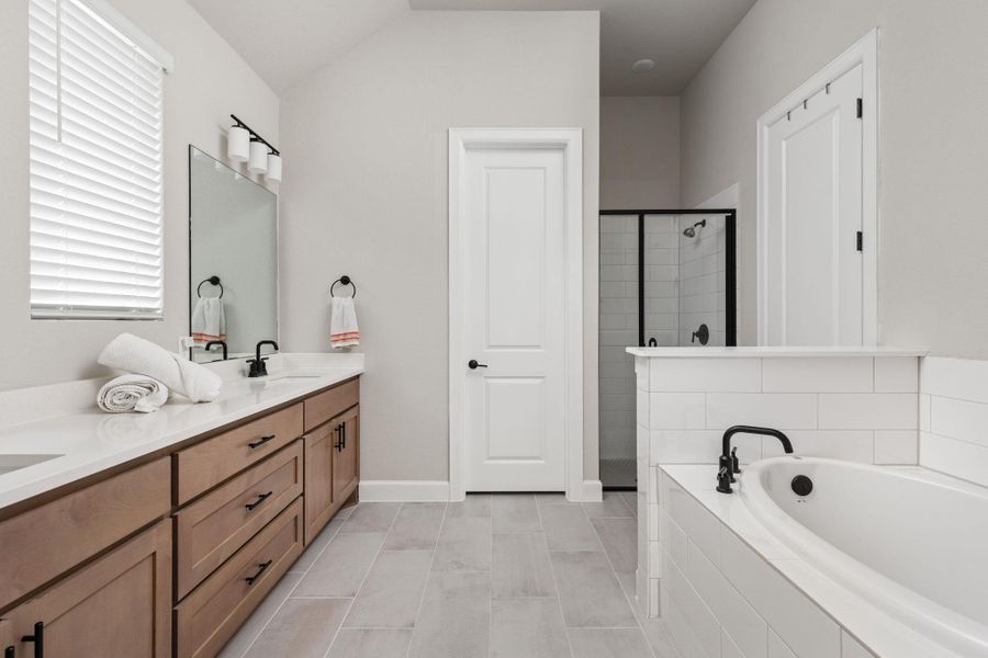 Full bathroom featuring double vanity, a bath, a shower stall, and light tile patterned floors