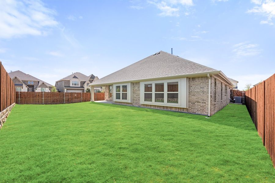 Brick home rear exterior with large fenced backyard and green lawn