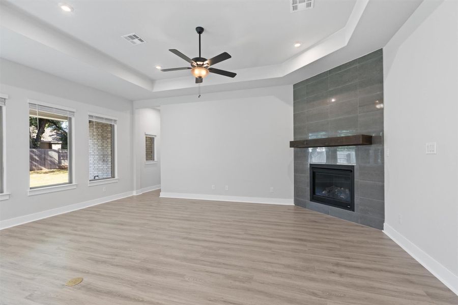 Unfurnished living room with a fireplace, light wood-type flooring, a ceiling fan, a raised ceiling, and recessed lighting