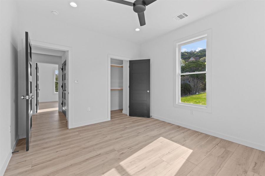 Unfurnished bedroom featuring light wood-style floors, ceiling fan, a spacious closet, recessed lighting, and multiple windows