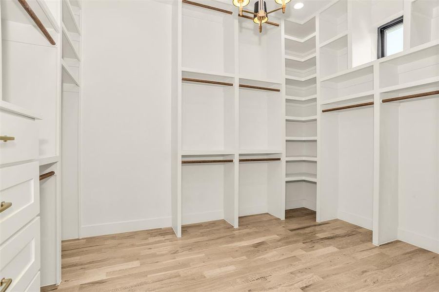 Spacious closet featuring light wood finished floors and a chandelier
