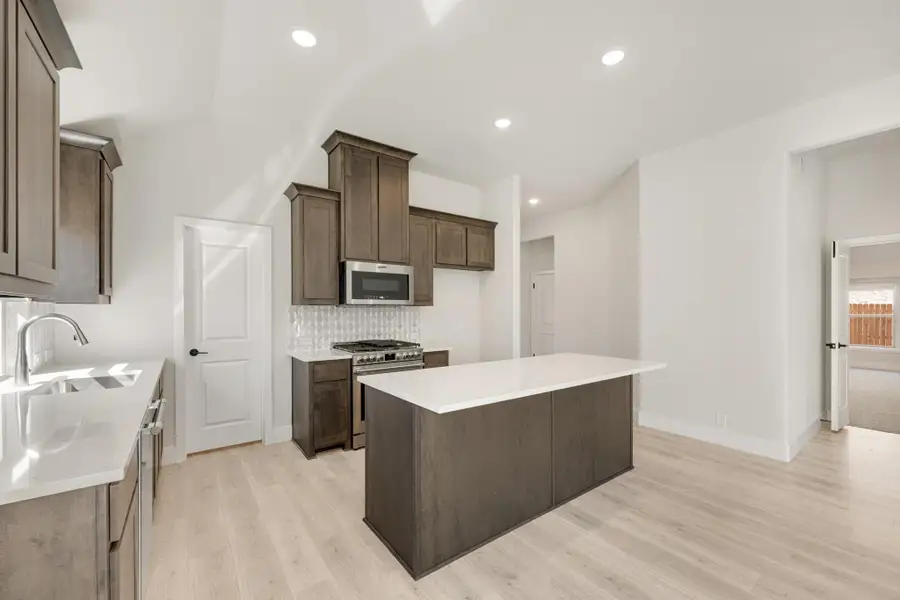 Kitchen with dark wood cabinets, center island, white countertops, and stainless steel appliances on light hardwood floors