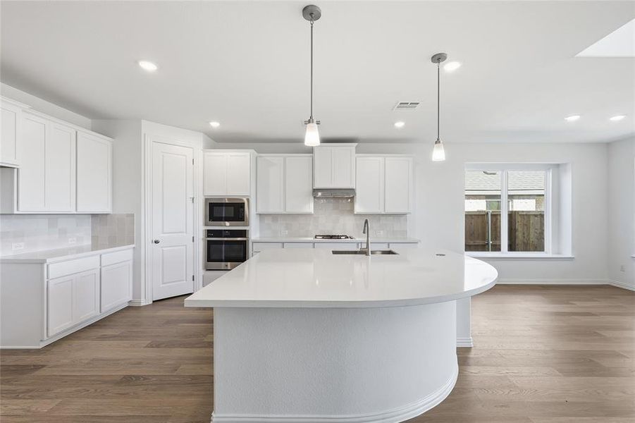 Kitchen featuring white cabinets, dark wood-type flooring, an island with sink, and stainless steel appliances