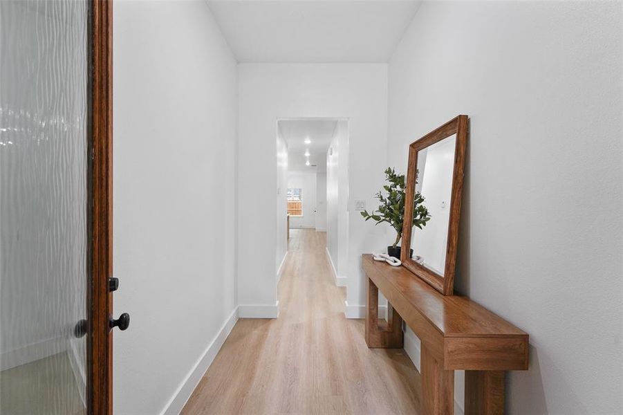 Entryway featuring a wood-finish door with textured glass, light wood-finish flooring, white walls, and an arched doorway opening to additional living spaces Entryway featuring a wood-finish door with textured glass, light wood-finish flooring, white walls, and an arched doorway opening to additional living spaces
