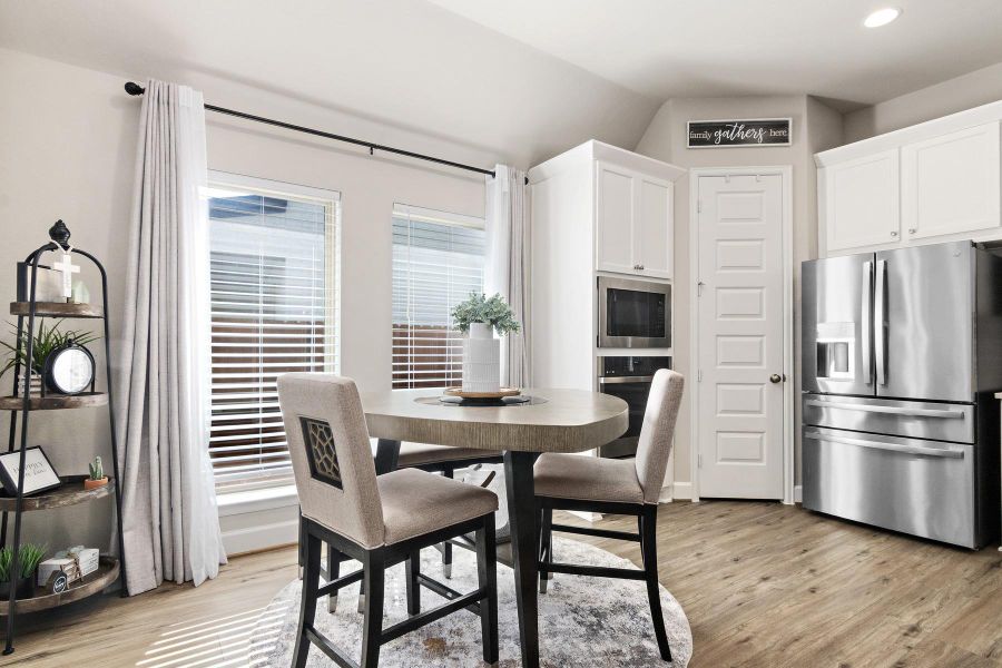 This kitchen features a modern design with stainless steel appliances, light wood flooring, and white cabinetry, large windows that provide natural light, accentuated by elegant drapes. A stylish shelving unit adds a decorative touch.
