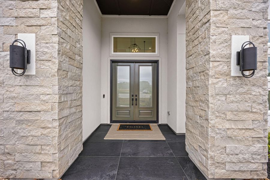 Welcome home! Before even entering the home, you are greeted with a welcoming and spacious front porch! A modern entryway with a sleek double door framed by large stone columns creating an inviting and elegant first impression.