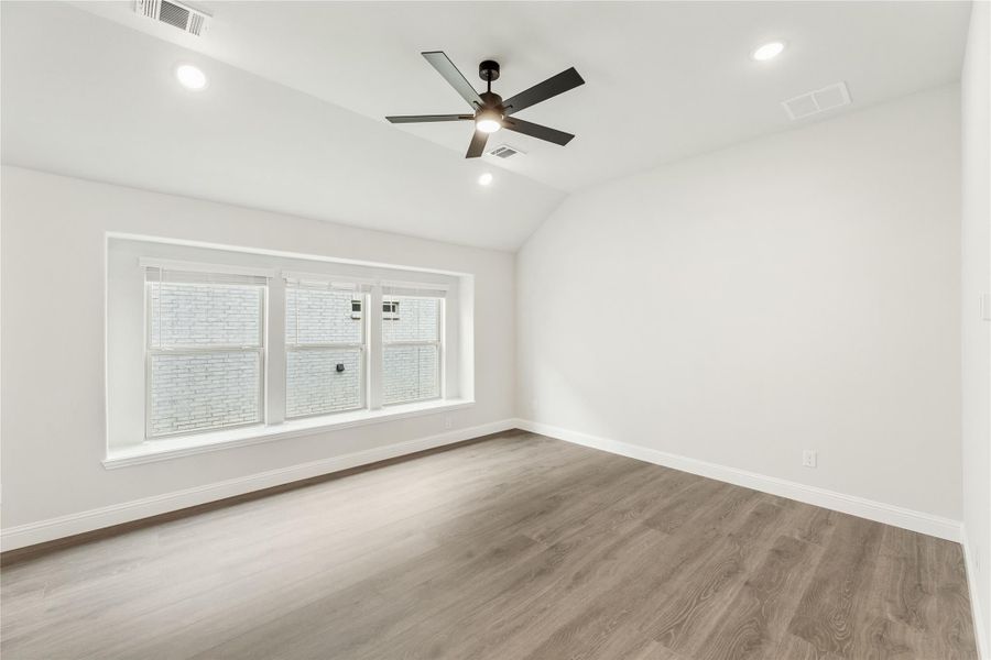 Empty room with hardwood floors, vaulted ceiling, ceiling fan, and large triple window Empty room with hardwood floors, vaulted ceiling, ceiling fan, and large triple window