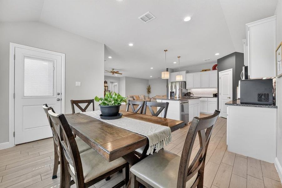 Open-concept dining area featuring wood-finish flooring, a white paneled door, and recessed lighting