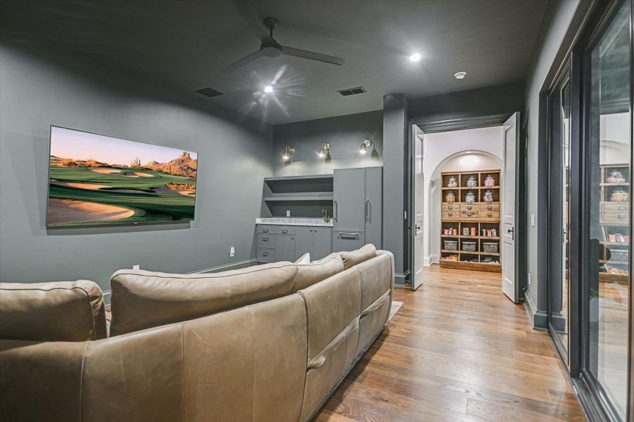 Home theater room with wood finished floors, ceiling fan, and arched walkways Home theater room with wood finished floors, ceiling fan, and arched walkways