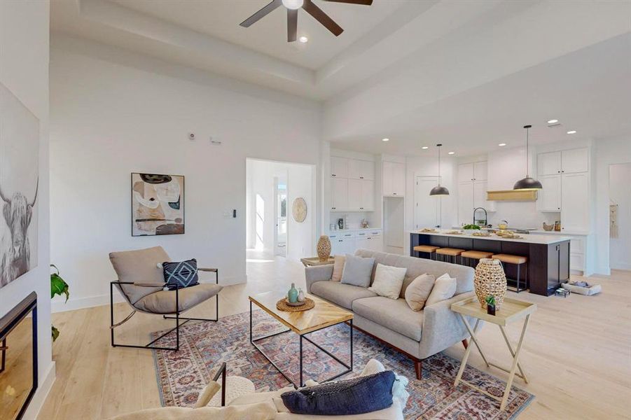 Living room with a high ceiling, light wood-type flooring, and ceiling fan