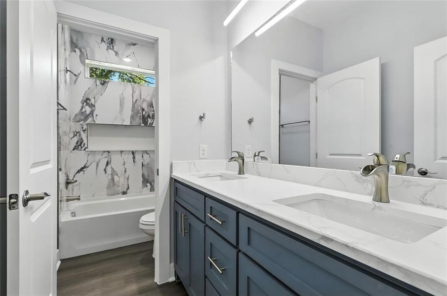 Full bath with double vanity, dark wood-style flooring, and shower / bath combination