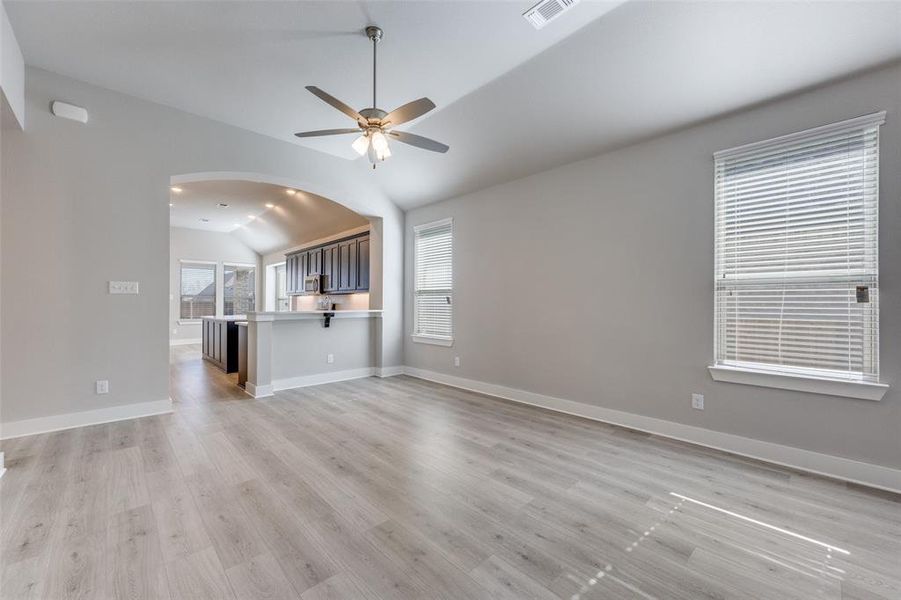 Unfurnished living room featuring lofted ceiling, light wood finished floors, a ceiling fan, healthy amount of natural light, and arched walkways