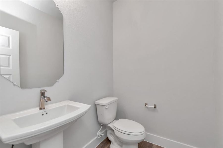 Immerse yourself in modern elegance within this delightful half bathroom. Featuring a sophisticated 5-panel door, upgraded pedestal sink, contemporary hardware, and stylish vanity lights, it exudes a sense of refinement. Sample photo of completed home. Actual colors and selections may vary.