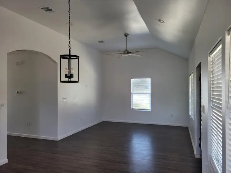 Unfurnished dining area featuring arched walkways, a ceiling fan, dark wood finished floors, lofted ceiling, and a chandelier