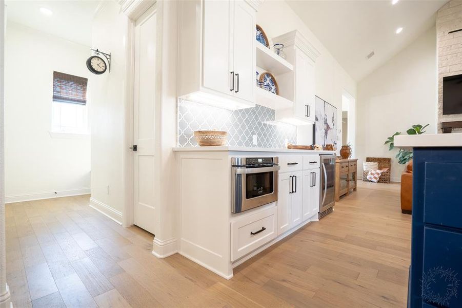 Kitchen featuring light countertops, light wood-style floors, white cabinets, stainless steel oven, and vaulted ceiling Kitchen featuring light countertops, light wood-style floors, white cabinets, stainless steel oven, and vaulted ceiling