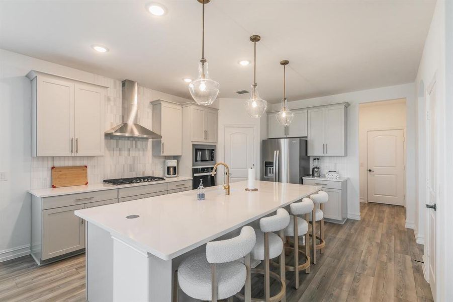 Kitchen featuring backsplash, stainless steel appliances, wall chimney exhaust hood, and an island with sink