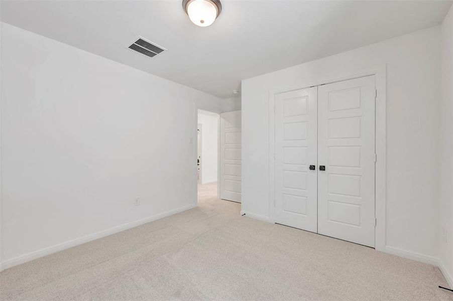 Carpeted room featuring white walls, a flush-mount ceiling light fixture, and a pair of paneled bifold closet doors with dark hardware