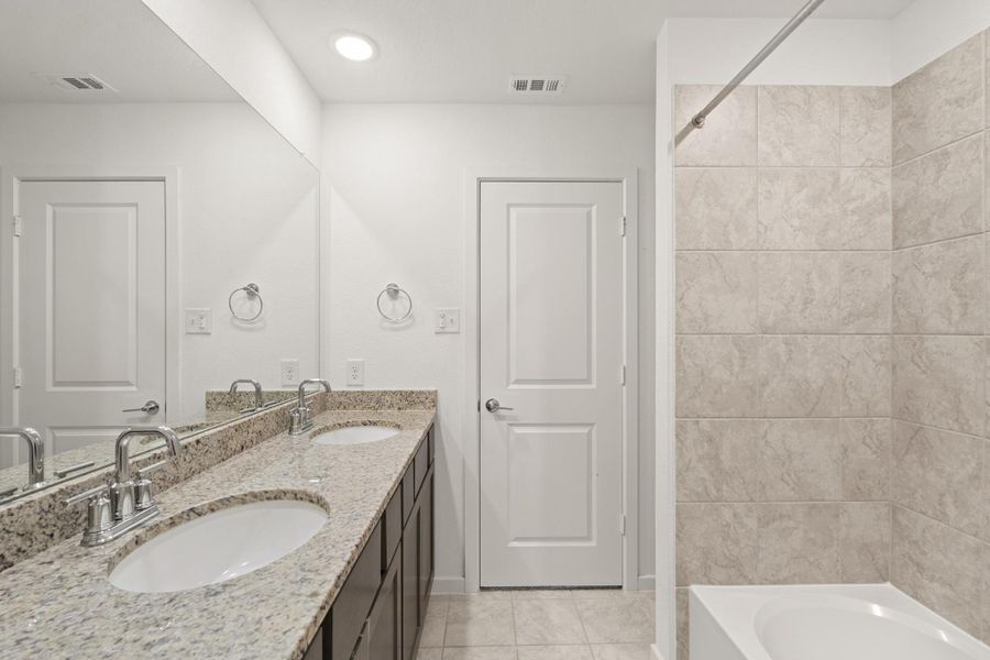 This full bathroom is located off the hall of the secondary bedrooms making it easy to share and get ready. It features a large vanity, dual sinks, wood cabinets, granite countertops, and a large combination tub and shower.