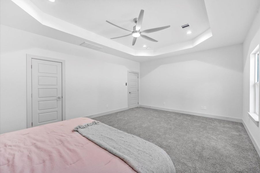 This primary spacious bedroom features a modern design with a tray ceiling and recessed lighting. It has large windows for natural light, a ceiling fan, and plush carpeting, creating a cozy and inviting atmosphere. This primary spacious bedroom features a modern design with a tray ceiling and recessed lighting. It has large windows for natural light, a ceiling fan, and plush carpeting, creating a cozy and inviting atmosphere.