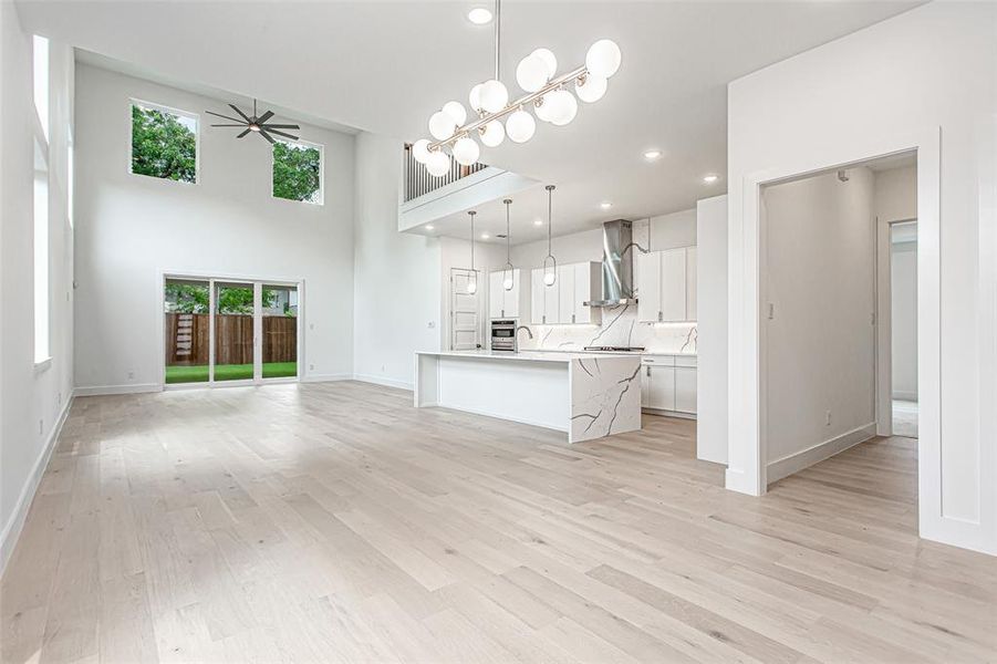 Unfurnished living room featuring a ceiling fan, light wood finished floors, baseboards, a chandelier, and recessed lighting