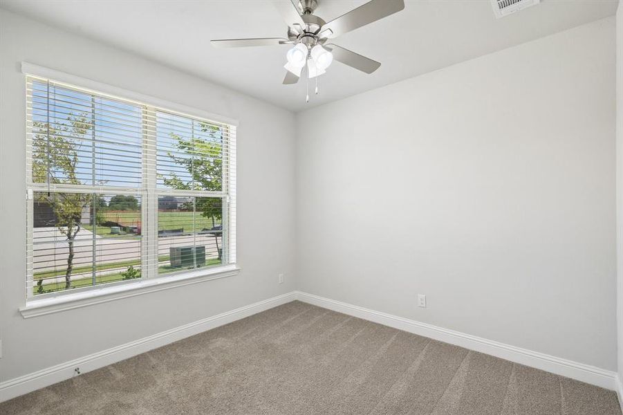 First floor secondary bedroom featuring a large window with horizontal blinds, a ceiling fan with light fixture, and white baseboards. Can also be used as an office First floor secondary bedroom featuring a large window with horizontal blinds, a ceiling fan with light fixture, and white baseboards. Can also be used as an office