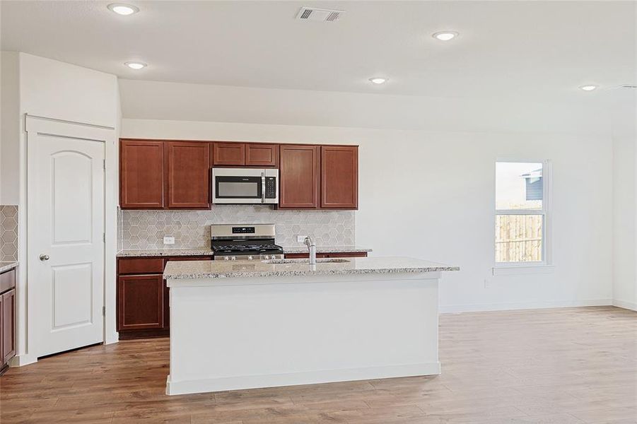 Kitchen with a center island with sink, light wood-type flooring, sink, and appliances with stainless steel finishes