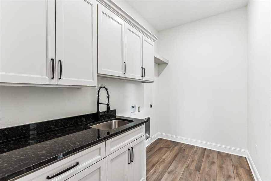 Laundry room with sink, dark stone counters, wood-type flooring, connecting off primary bath