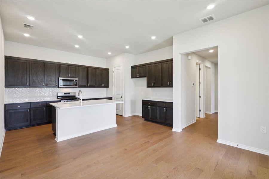 Kitchen featuring backsplash, recessed lighting, stainless steel appliances, a center island with sink, and dark brown cabinetry Kitchen featuring backsplash, recessed lighting, stainless steel appliances, a center island with sink, and dark brown cabinetry