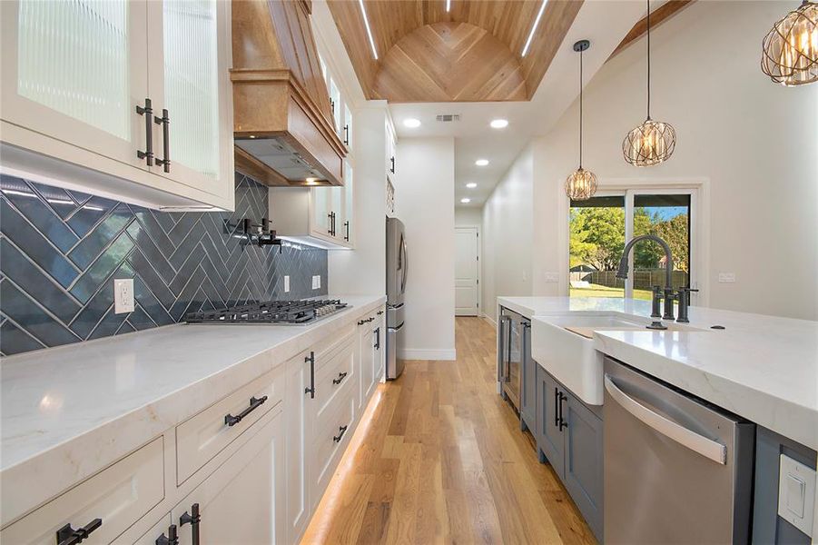 Kitchen with light stone countertops, hanging light fixtures, glass insert cabinets, light wood-type flooring, and white cabinetry