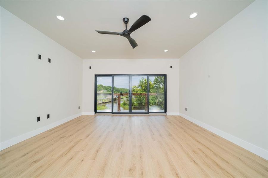 Spacious room featuring wood-finish flooring, a contemporary ceiling fan, recessed lighting, and expansive sliding glass doors that open to a balcony overlooking a body of water