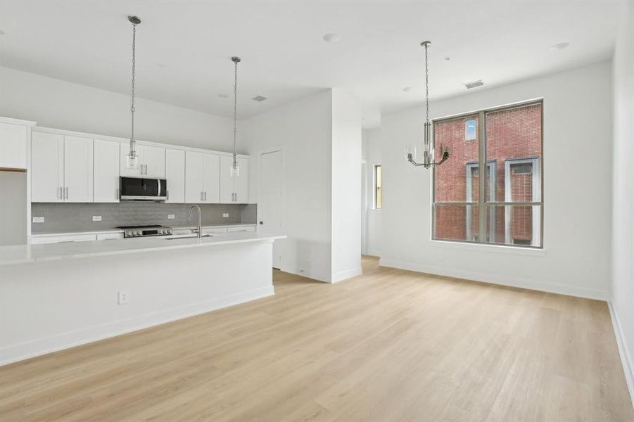 Kitchen with appliances with stainless steel finishes, white cabinets, light countertops, tasteful backsplash, and light wood finished floors