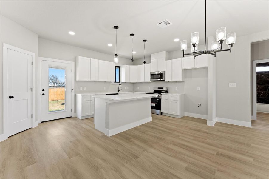 Kitchen featuring stainless steel appliances, white cabinetry, a center island, light wood-type flooring, and hanging lights