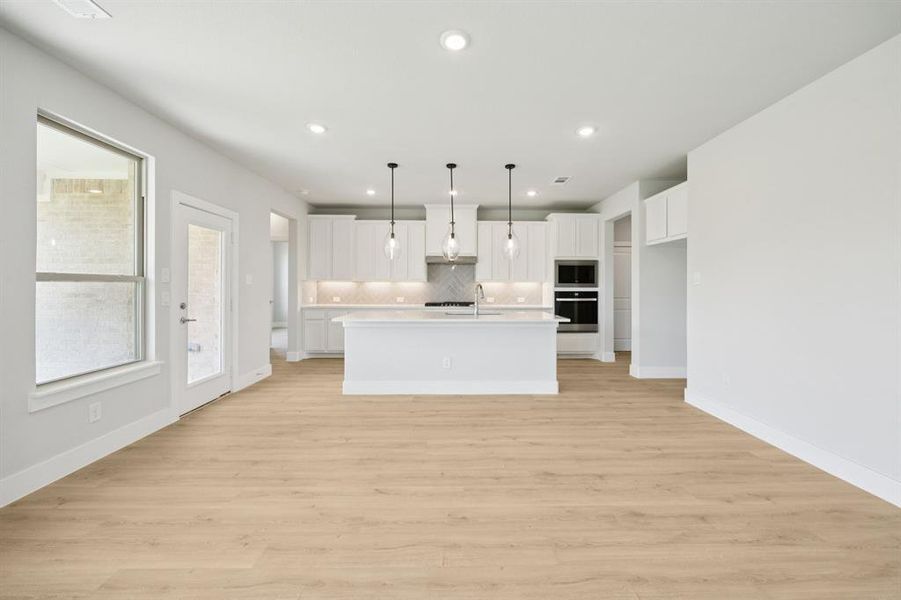 Kitchen featuring white cabinetry, a kitchen island with sink, decorative backsplash, decorative light fixtures, and light wood-style floors