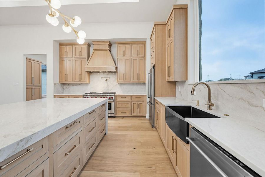 Contemporary kitchen featuring light wood-finish cabinetry, white marble countertops, a large center island, built-in stainless steel appliances, and wood-finish flooring
