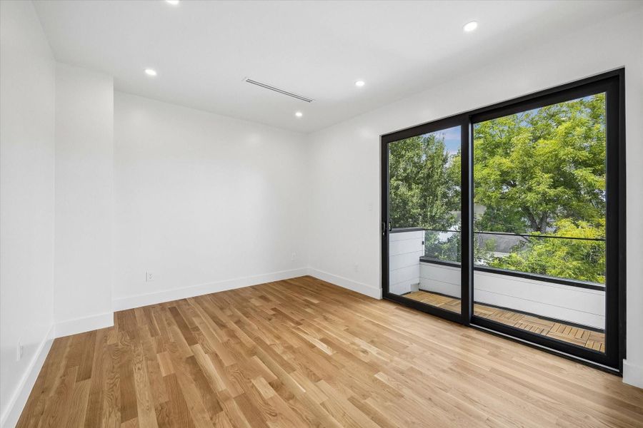 Bright and spacious room with hardwood floors, large sliding glass doors, and a private balcony offering a view of greenery. Bright and spacious room with hardwood floors, large sliding glass doors, and a private balcony offering a view of greenery.
