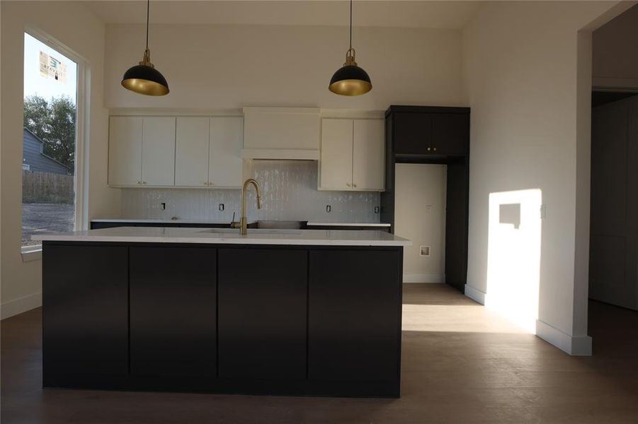 Kitchen with decorative backsplash, pendant lighting, a center island with sink, light stone countertops, and dark wood finished floors