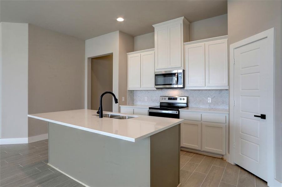 Kitchen with white cabinetry, appliances with stainless steel finishes, sink, and a center island with sink