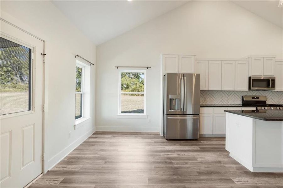 Kitchen featuring white cabinets, appliances with stainless steel finishes, backsplash, high vaulted ceiling, and light wood-style floors