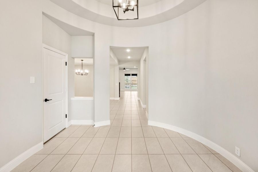 Curved entryway with tray ceiling, black chandelier, tile floors, and hallway leading to main living area Curved entryway with tray ceiling, black chandelier, tile floors, and hallway leading to main living area