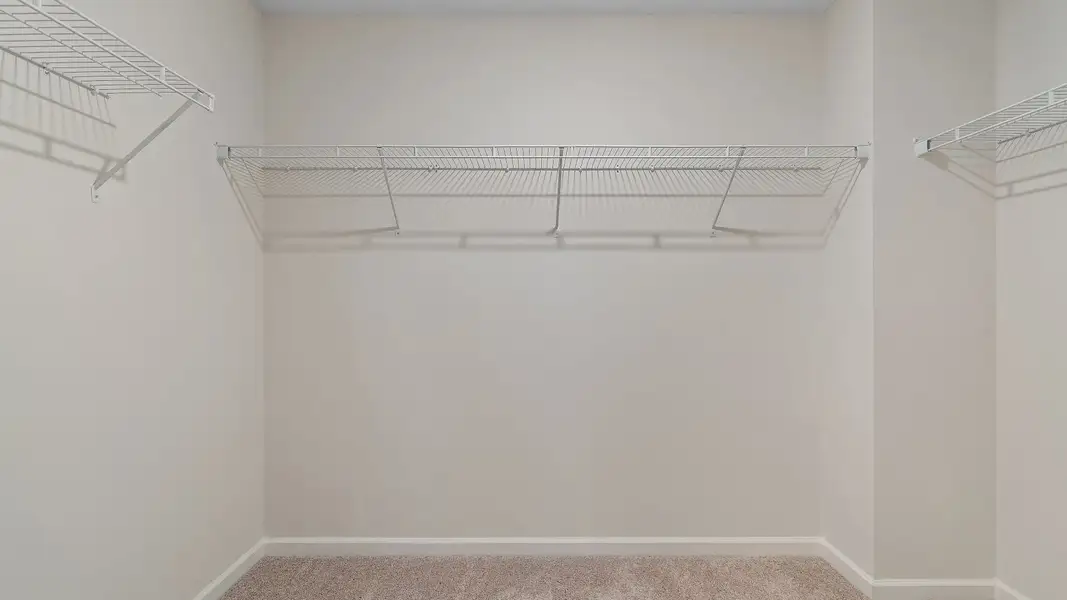Generous walk-in closet with built-in shelves, hanging rods, and storage space in new construction townhome.