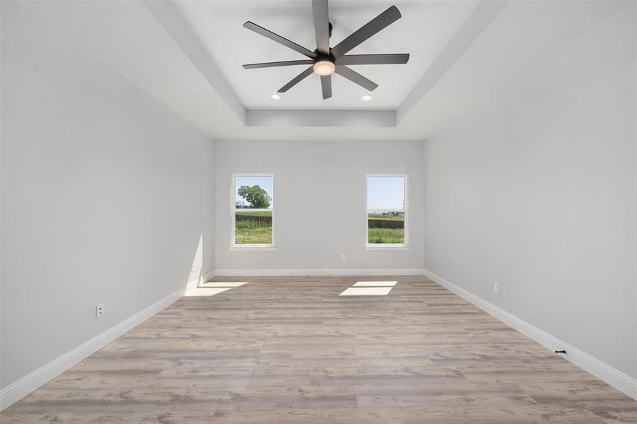 Spare room featuring a tray ceiling, baseboards, recessed lighting, light wood-style floors, and ceiling fan
