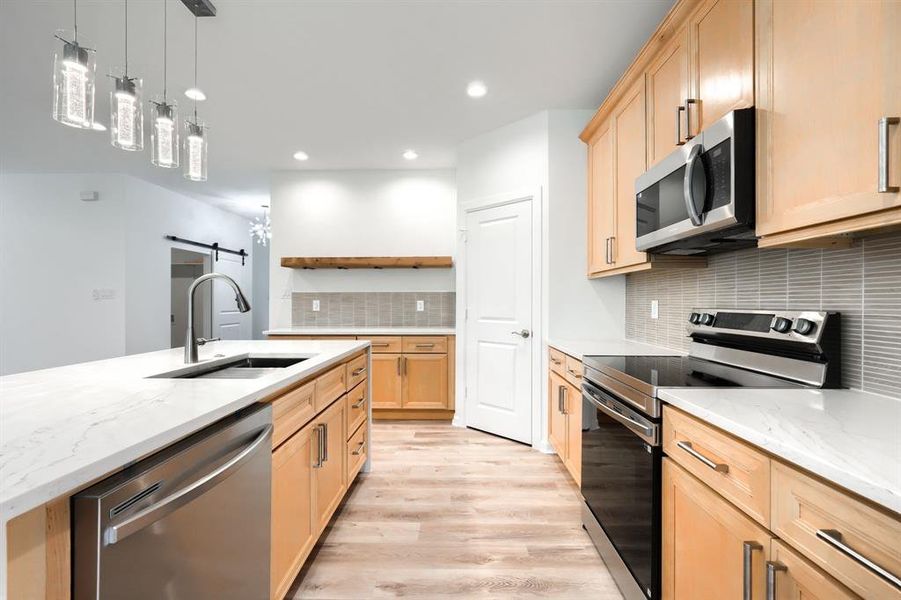 Kitchen featuring stainless steel appliances, a barn door, light stone countertops, hanging light fixtures, and backsplash