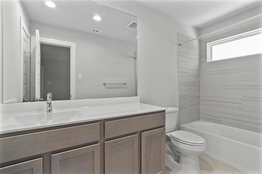 Secondary bath features tile flooring, bath/shower combo with tile surround, stained cabinets, beautiful light countertops, mirror, sleek fixtures and modern finishes.