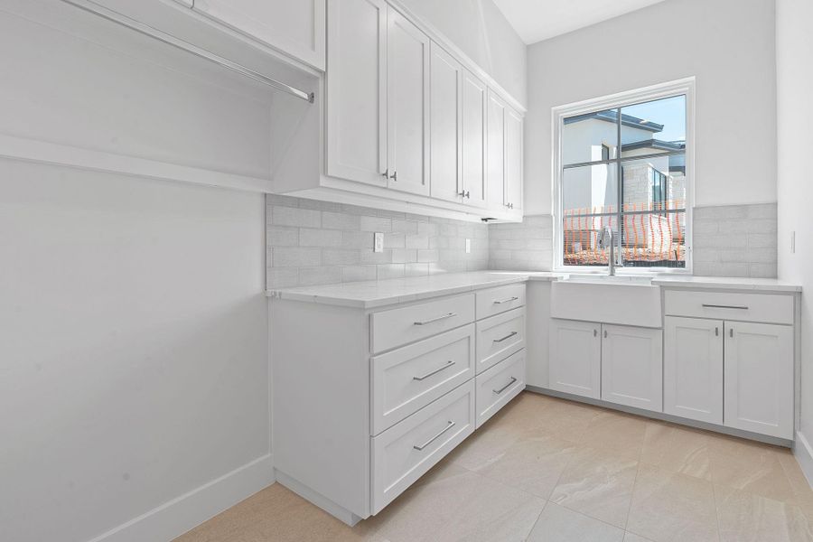 Laundry room with a sink, room for 2nd Refrigerator, light Quartz counters, decorative backsplash, and white cabinetry Laundry room with a sink, room for 2nd Refrigerator, light Quartz counters, decorative backsplash, and white cabinetry