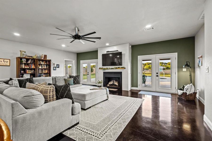 Living area featuring french doors, recessed lighting, a fireplace, concrete floors, and a ceiling fan Living area featuring french doors, recessed lighting, a fireplace, concrete floors, and a ceiling fan