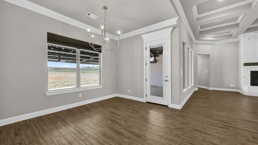 Unfurnished dining area featuring coffered ceiling, dark hardwood / wood-style flooring, ornamental molding, a brick fireplace, and a chandelier