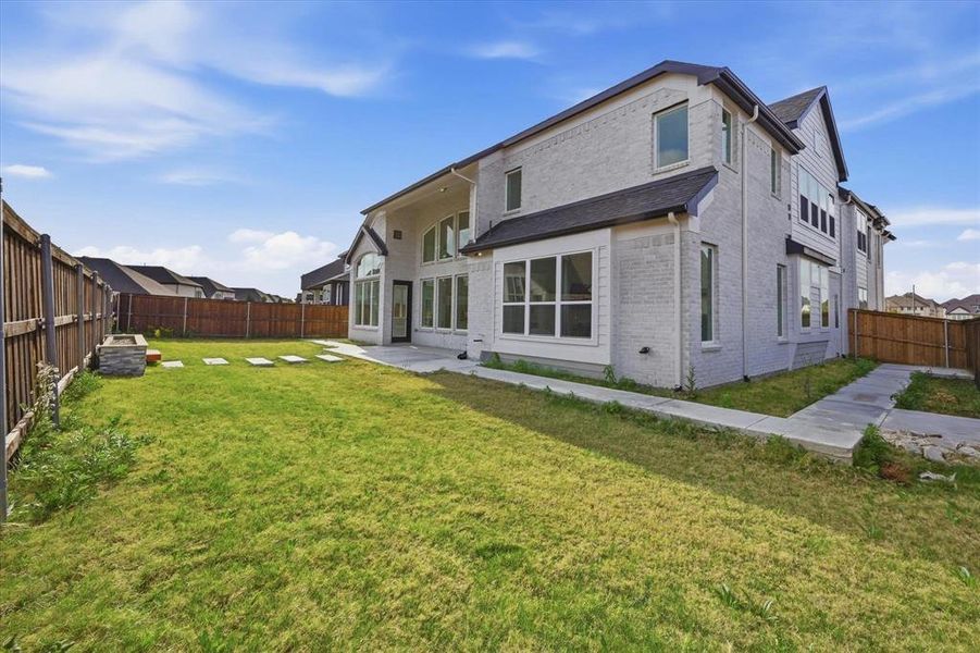 Spacious rear yard with a perimeter wood fence, paver patio, and stone fire pit