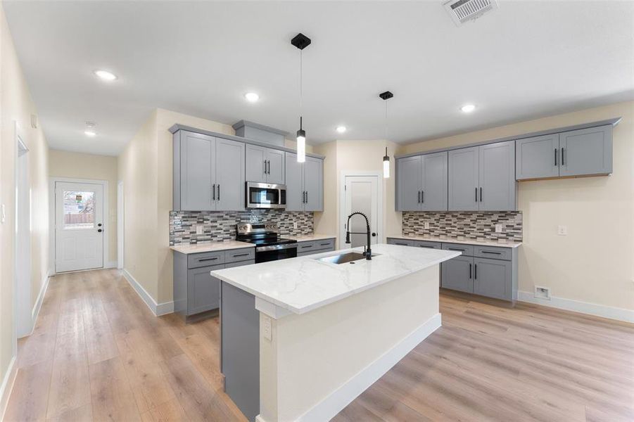 Kitchen featuring appliances with stainless steel finishes, pendant lighting, sink, a kitchen island with sink, and light stone countertops