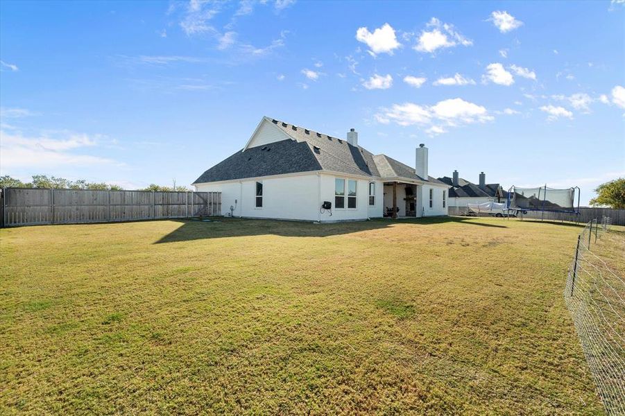 Rear view of property with a fenced backyard, a chimney, a trampoline, a patio, and a shingled roof