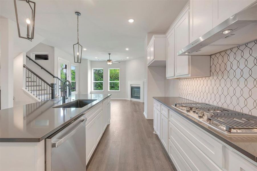 Contemporary kitchen featuring white cabinetry, dark countertops, and a gas cooktop with a stainless steel range hood Contemporary kitchen featuring white cabinetry, dark countertops, and a gas cooktop with a stainless steel range hood